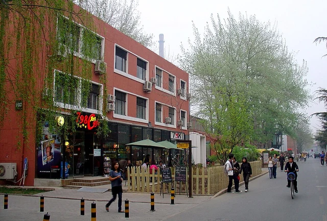 Visitors walking past red-brick buildings and art shops in Beijing's 798 Art District.