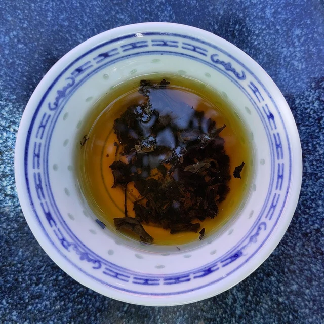 Anhua dark tea brewed in a porcelain cup, with tea leaves in the amber liquid.