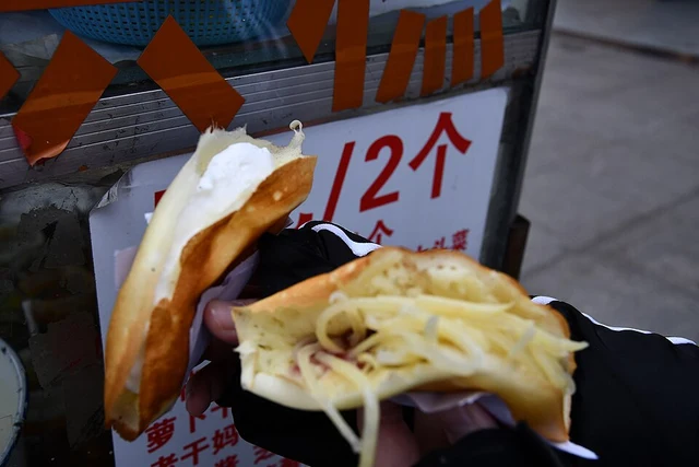 Filled Chengdu danhonggao egg pancakes held beside a street stall.