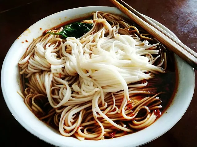 A bowl of plain Chongqing xiaomian with greens, chilli-seasoned sauce and chopsticks.