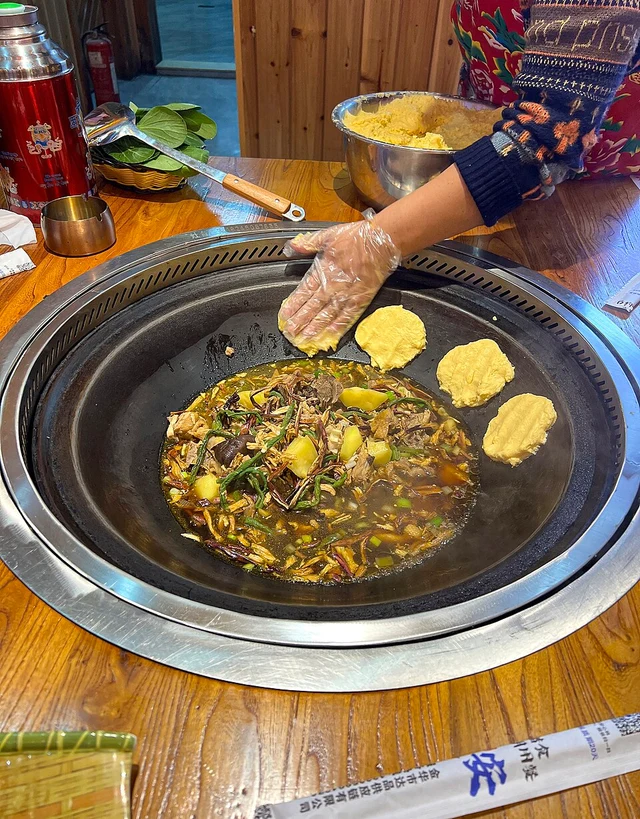 A server putting corn dough on the side of an iron-pot stew in Hengdian, Zhejiang, in January 2025.