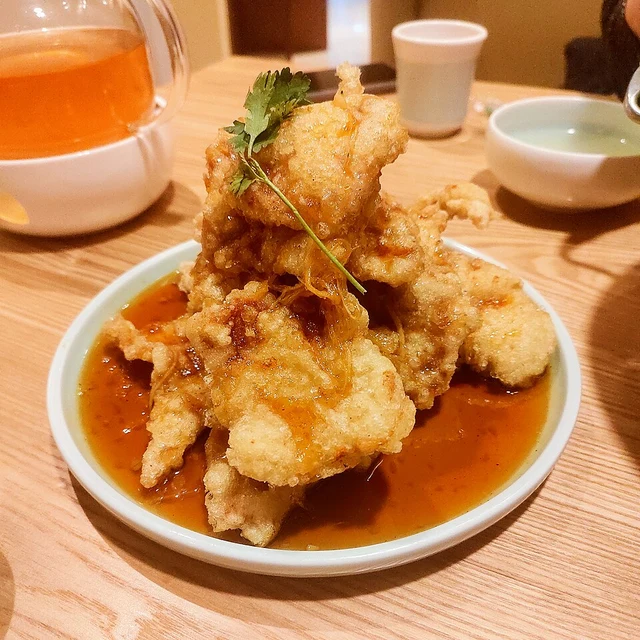 Golden battered slices of guobaorou with sauce on a white plate.
