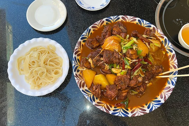Dapanji with potatoes and peppers beside a plate of wide noodles in Kashgar in September 2023.