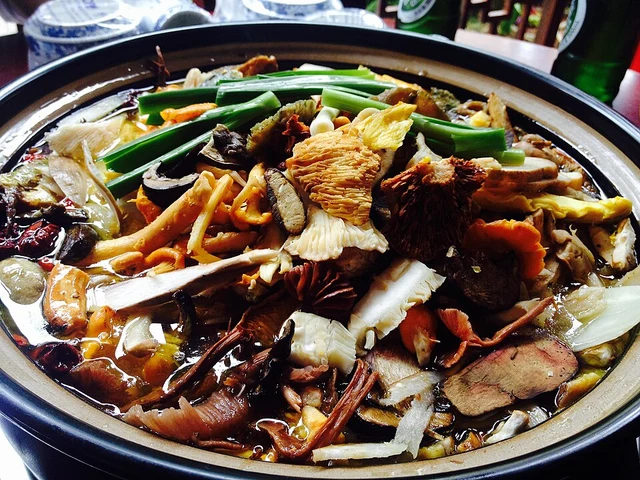 A mixed-mushroom hotpot with vegetables in a metal pot.