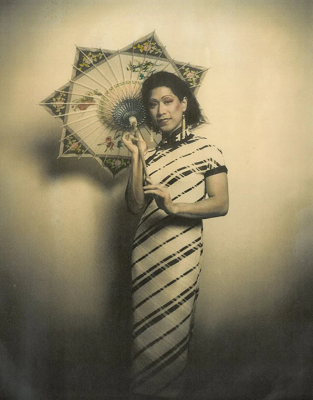 A hand-coloured archival photograph of a woman in Shanghai wearing a qipao and holding a parasol, circa the 1930s.