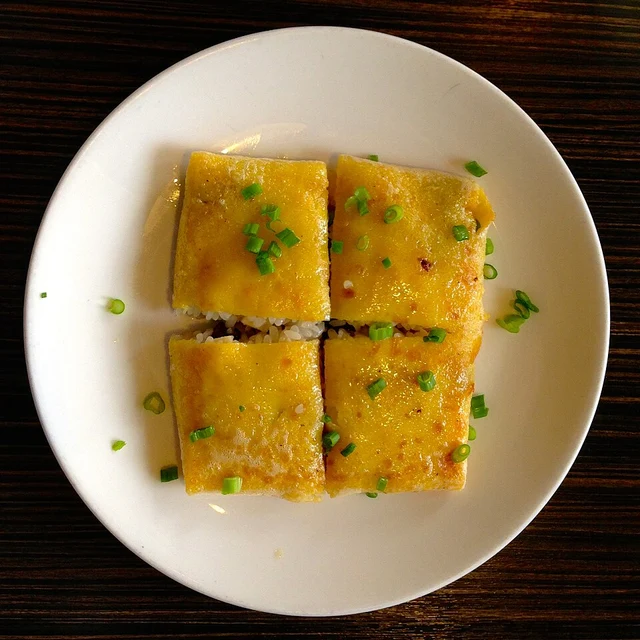 Four golden doupi pieces with chopped spring onions on a white plate.