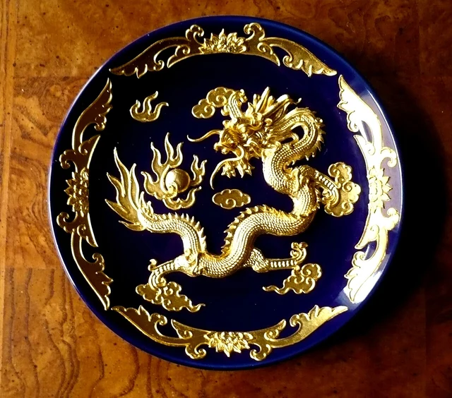 An Xiamen lacquer-thread plate with raised golden dragon decoration on a dark background.