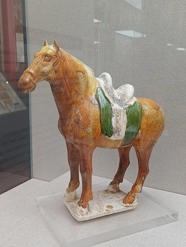 A Tang-dynasty sancai glazed horse displayed in a museum case.