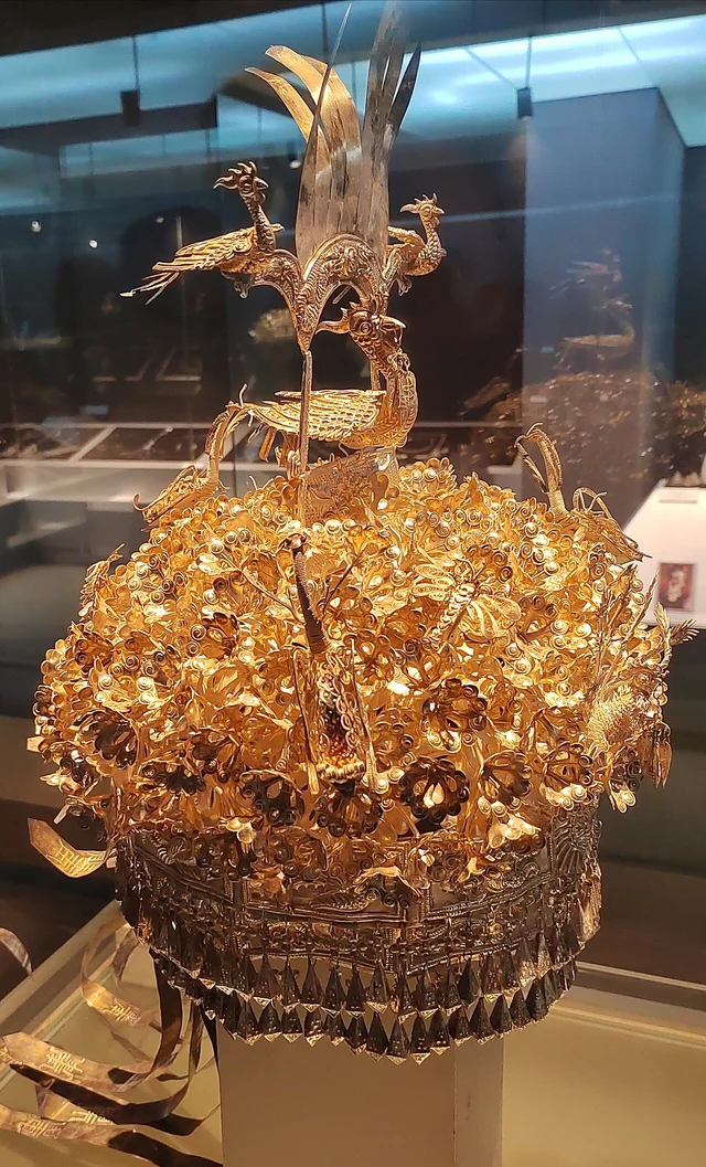 An ornate metal Miao headdress from Kaitang, Huangping, displayed in a museum case.