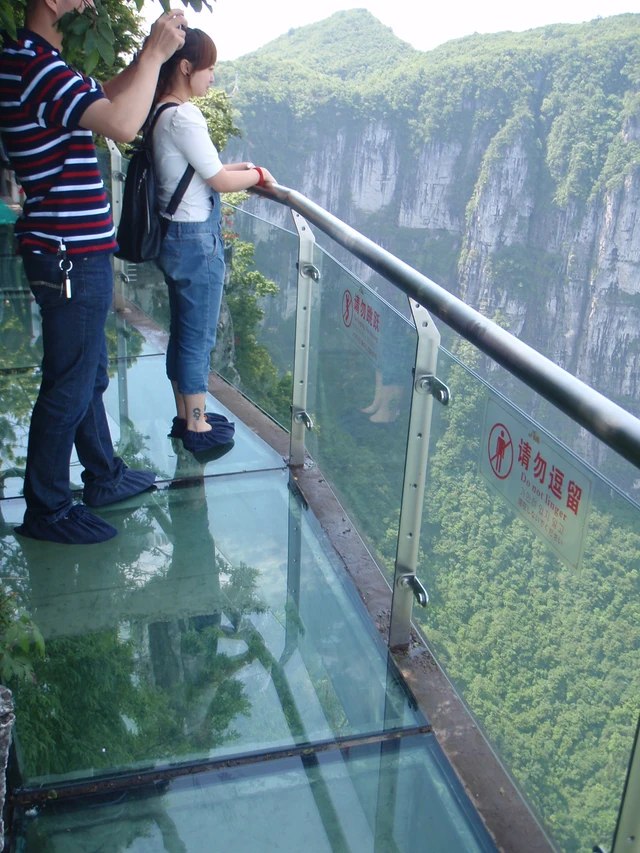 Visitors standing on the transparent glass walkway against a cliff at Tianmen Mountain.