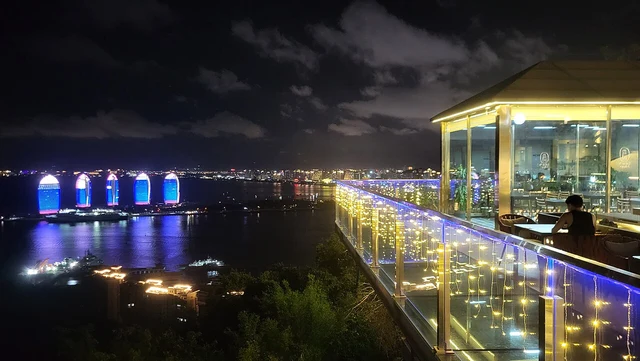 Sanya’s coast and city lights seen from a lit terrace at Luhuitou; a historical night photograph.