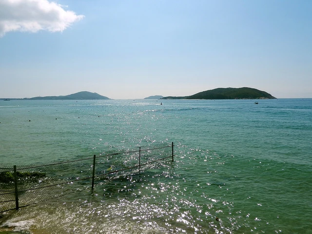 Turquoise sea and distant islands viewed past a waterfront railing at Yalong Bay; a historical photograph.