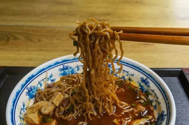 Changwang egg noodles lifted with chopsticks from a bowl of red broth, in the 2021 Pictures of Guizhou report.