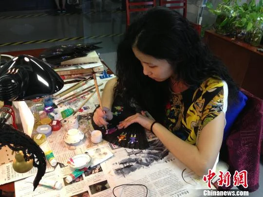 Wangxingji artisan Hu Lei painting a black folding fan at a workbench in 2013.