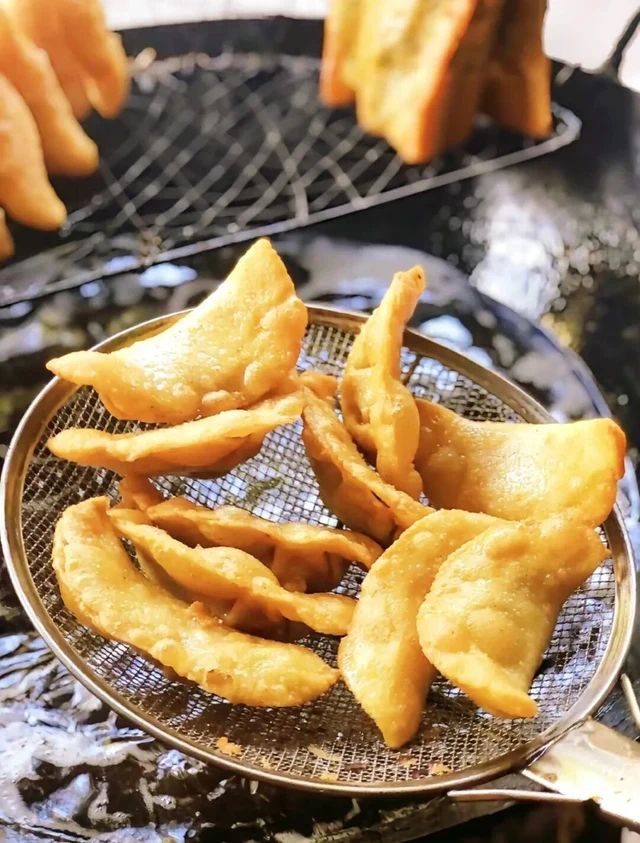 Golden Sanhe rice-flour dumplings drain on a wire skimmer over frying oil, in a 2026 photograph credited to Sanhe Ancient Town tourism.