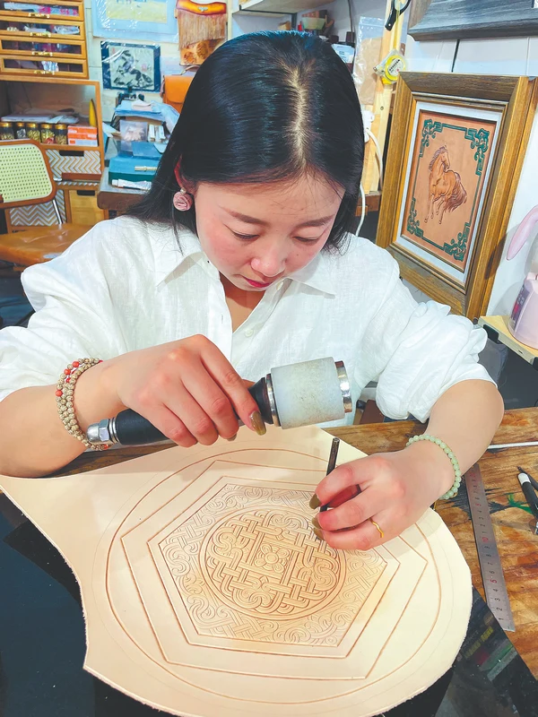 Li Xiaofang engraves a leather panel at her Hohhot studio in a China Daily photograph published in April 2025.