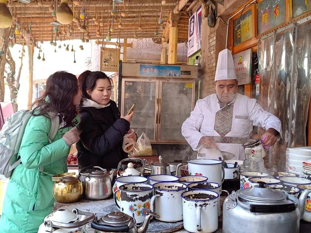 Visitors watching Kashgar jar-meat preparation with enamel mugs at Abu Grandpa's shop in January 2025.