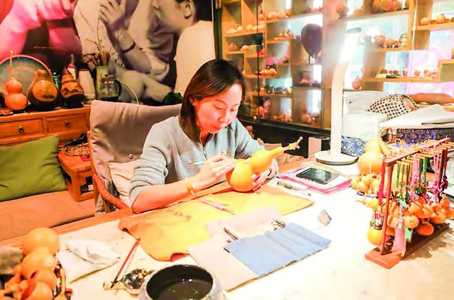 Ruan Xiyue carves a gourd at her Lanzhou studio on 11 May 2024, surrounded by decorated gourds; photograph by Ma Sha/Xinhua.