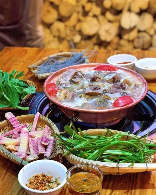 Lijiang cured pork-rib hotpot in a red pot, surrounded by vegetables and dipping sauce.