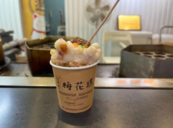 A freshly made Jiangnan plum-blossom cake with rice-ball toppings in a paper cup beside its mould.