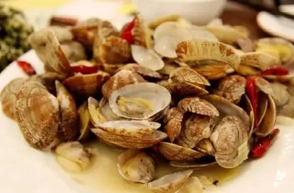 Qingdao-style stir-fried clams in the official August 2020 Qingdao–Anshun food feature, with shells and red and green garnish visible.