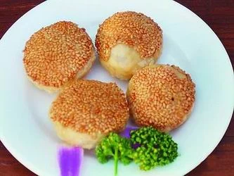 Four golden sesame-coated xiekehuang pastries on a white plate.
