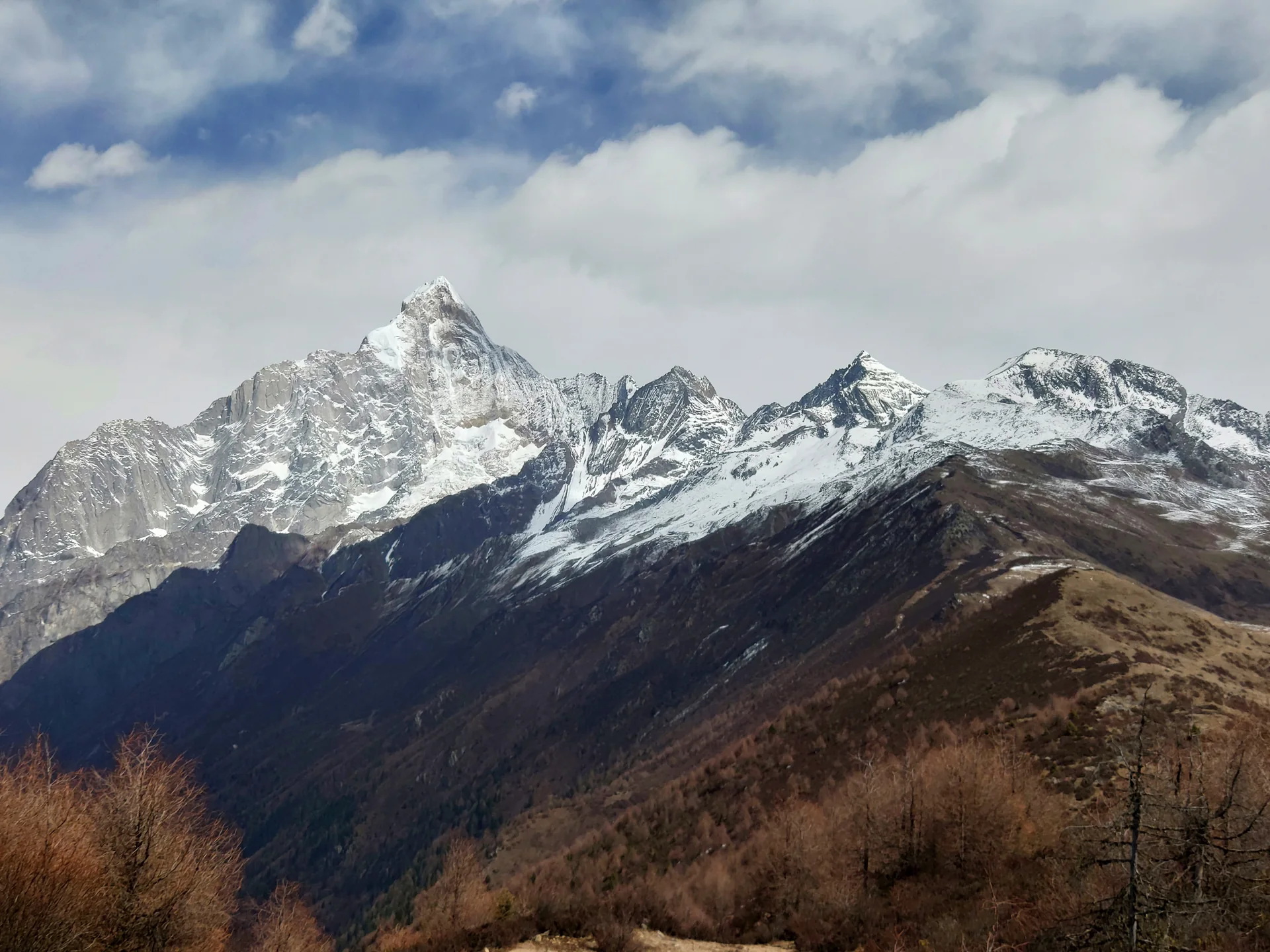 Snow-covered peaks of Mount Siguniang above forested ridges